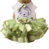 Dog wearing green tutu and white shirt.